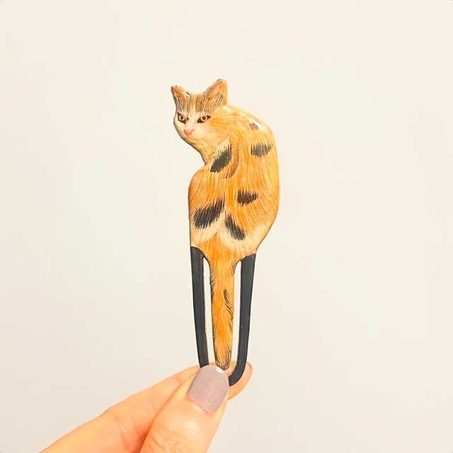ポケットの上に座る三毛猫の木製ブローチ