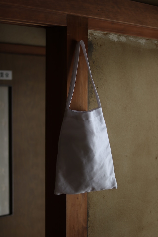白い生地で作られた、とてもシンプルなデザインのストックバッグが、古民家の風情ある壁にぶら下がっています。