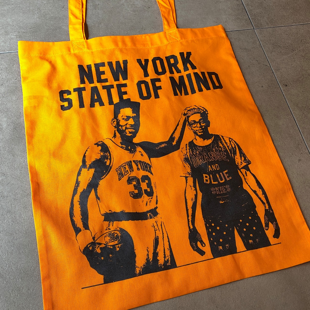 THE CITY NEVER STOPPED BELIEVING TOTE BAG ORANGE