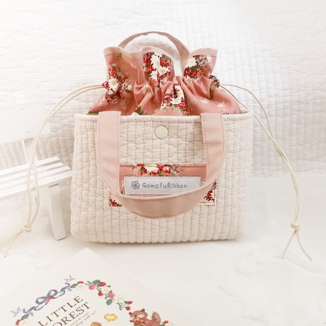 ヌビキルトのあおりポケット付き巾着ポーチ　くすみピンク色の生地にマーガレットと赤いお花　グレーのギンガムチェック　デザインタグ