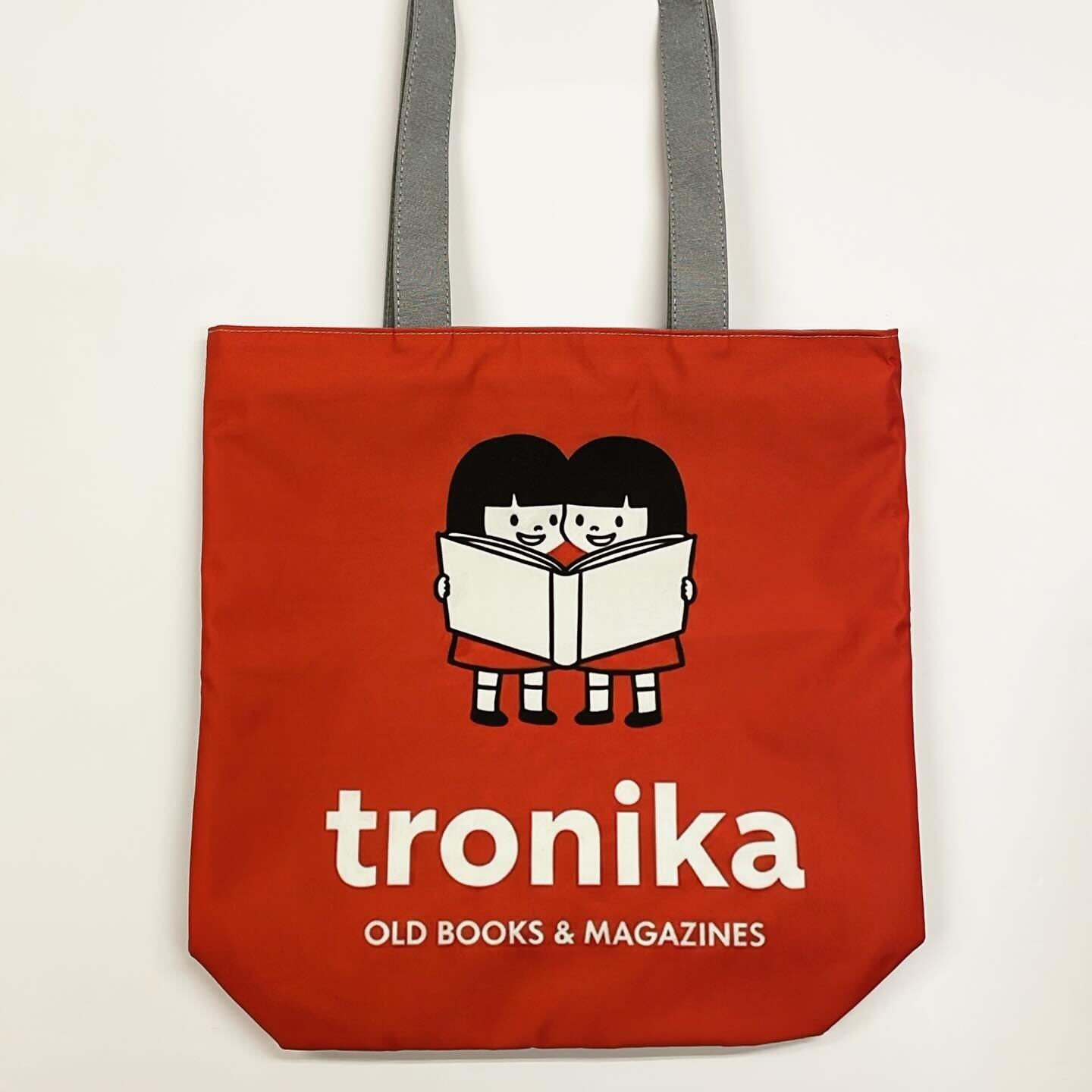 トートバッグ「トロニカ　双子イラスト　一緒に大きい本を読む　背景赤　裏面グレー」 - 画像1