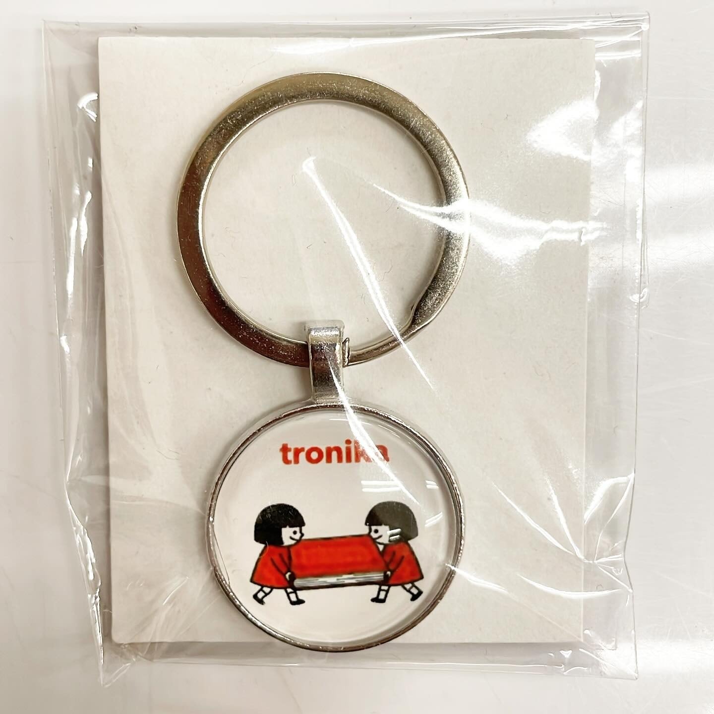 キーホルダー「トロニカ　双子　イラスト　大きい本を運ぶ」 - 画像1