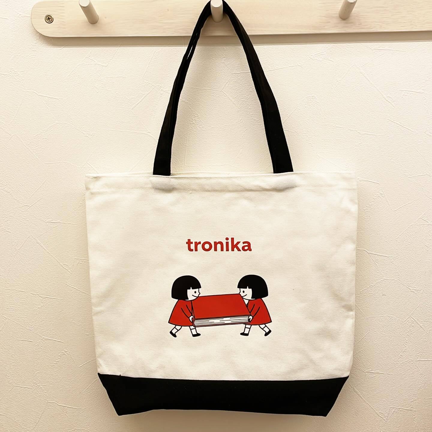 トートバッグ「トロニカ　双子イラスト　大きい本を運ぶ　白　持ち手黒　底黒」 - 画像1