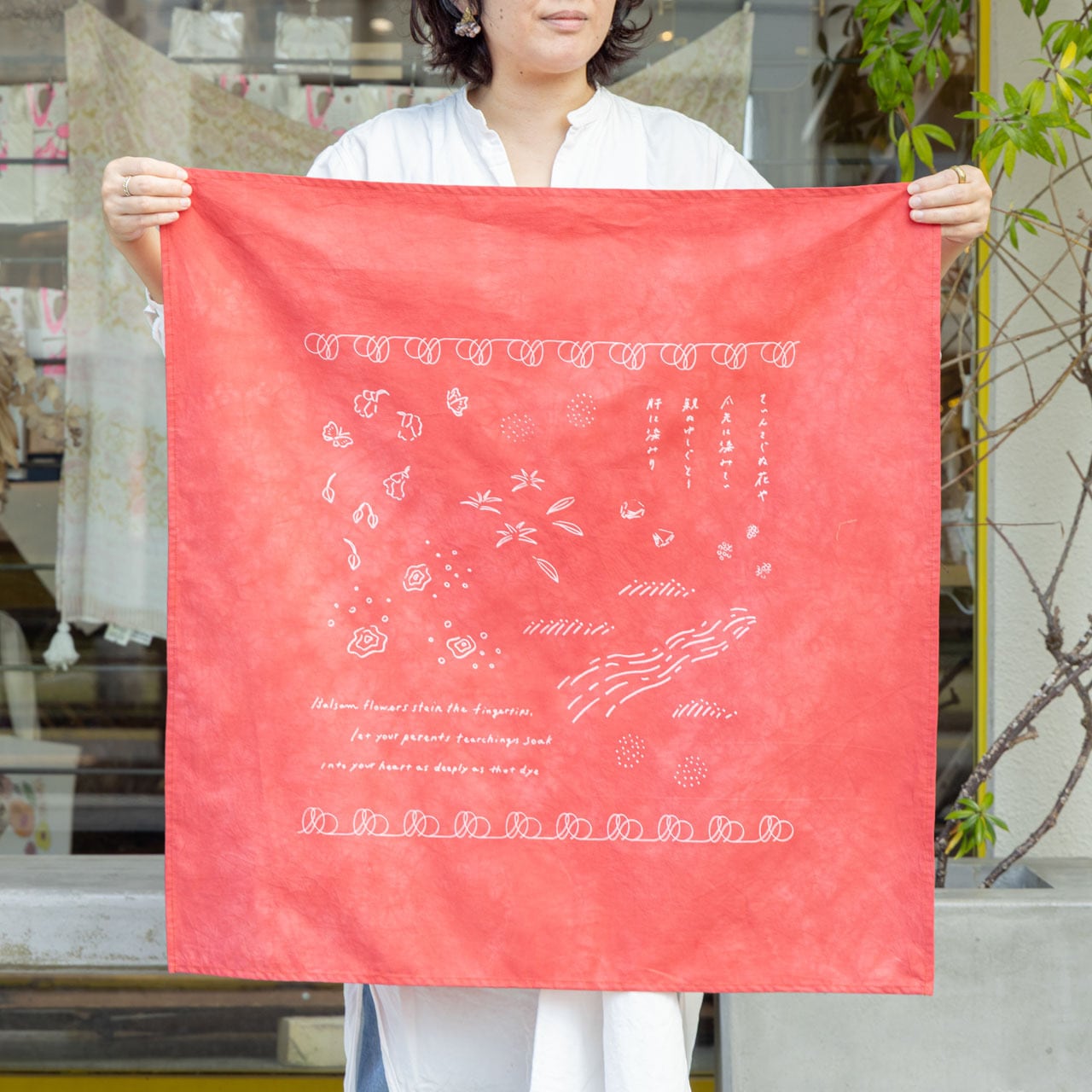 沖縄に育つ草花から抽出した染料で1枚ずつ草木染めを施した生地に、沖縄の民謡「てぃんさぐぬ花」の歌詞を重ねてプリントしたスカーフ。大判なのでファッションのアクセントになるだけでなく、時にはさっと荷物を包むのにも便利です。