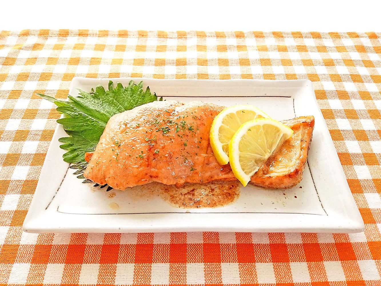 白い皿に盛られた焼き鮭に、大葉と輪切りのレモンを添えた一皿