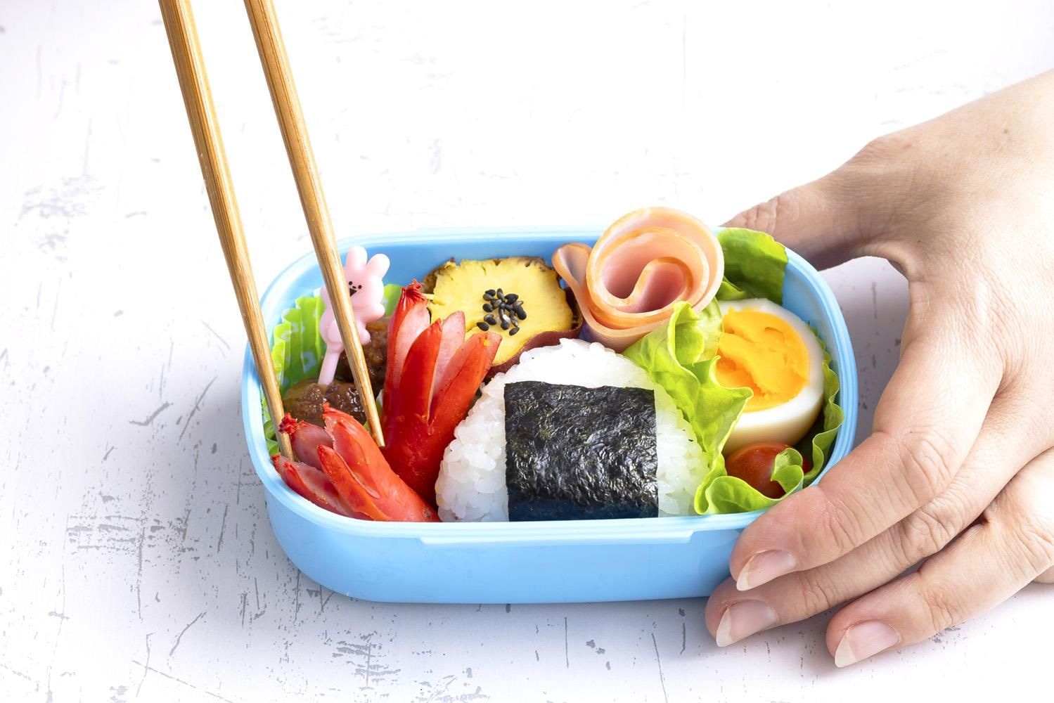 おにぎりやおかずを詰めたお弁当箱を手に持つ様子