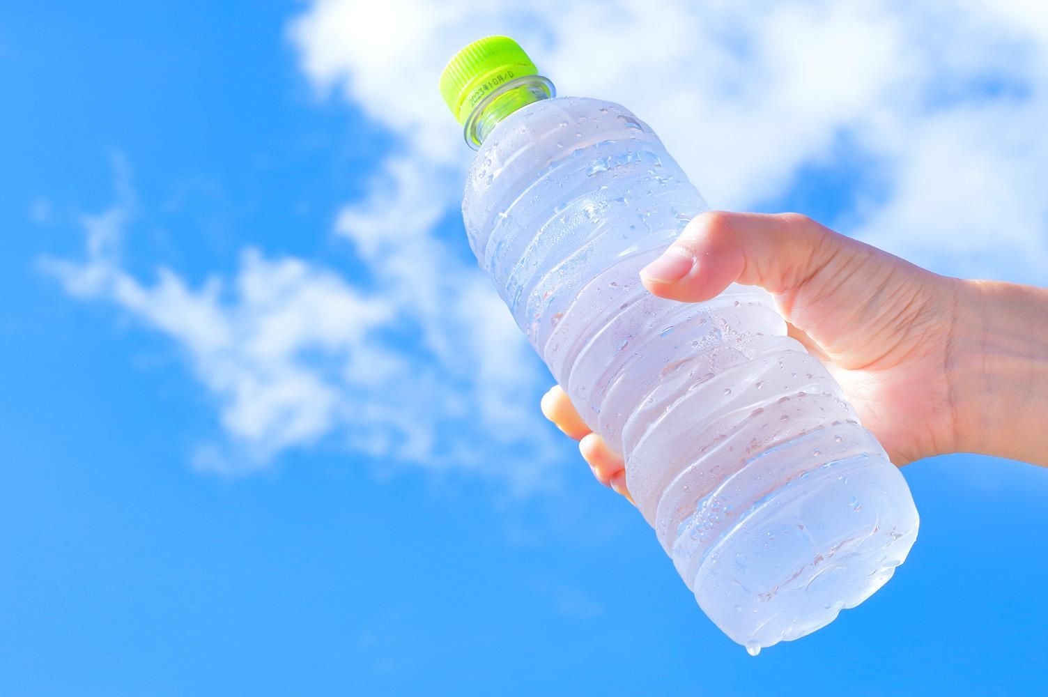 青空を背に、しずくのついた冷たいペットボトルの水を手に持っている様子