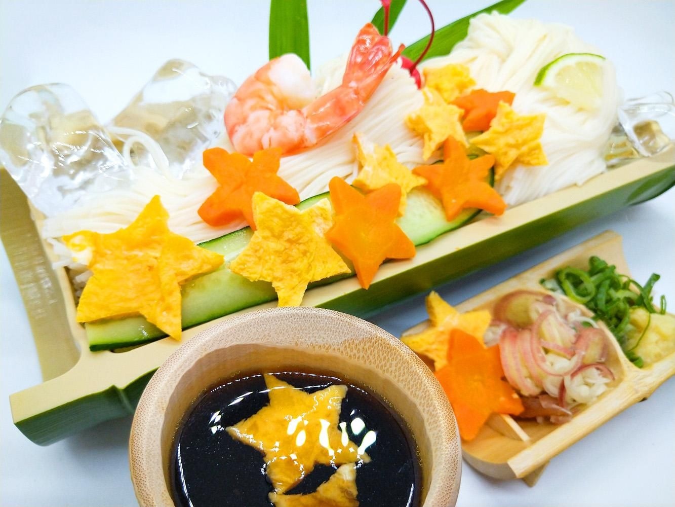 竹の器に氷とともに盛ったそうめんに、星形のにんじんや卵やきゅうり・えびを添え、つゆと薬味を並べた七夕の盛り合わせ
