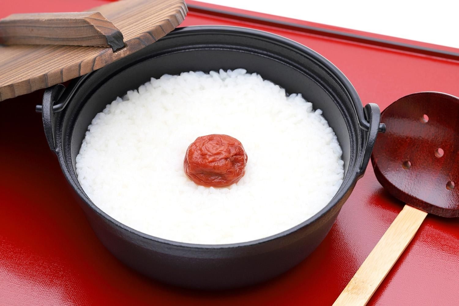 黒い鉄釜に炊きたての白いごはん。真ん中に赤い梅干しがのっている