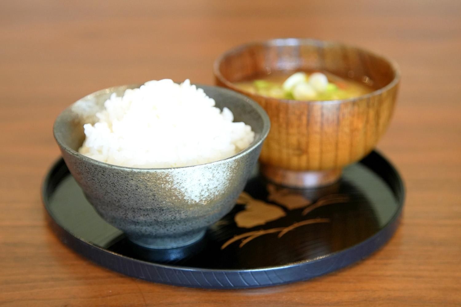黒いお盆に並ぶ白いごはんと木椀の温かい味噌汁