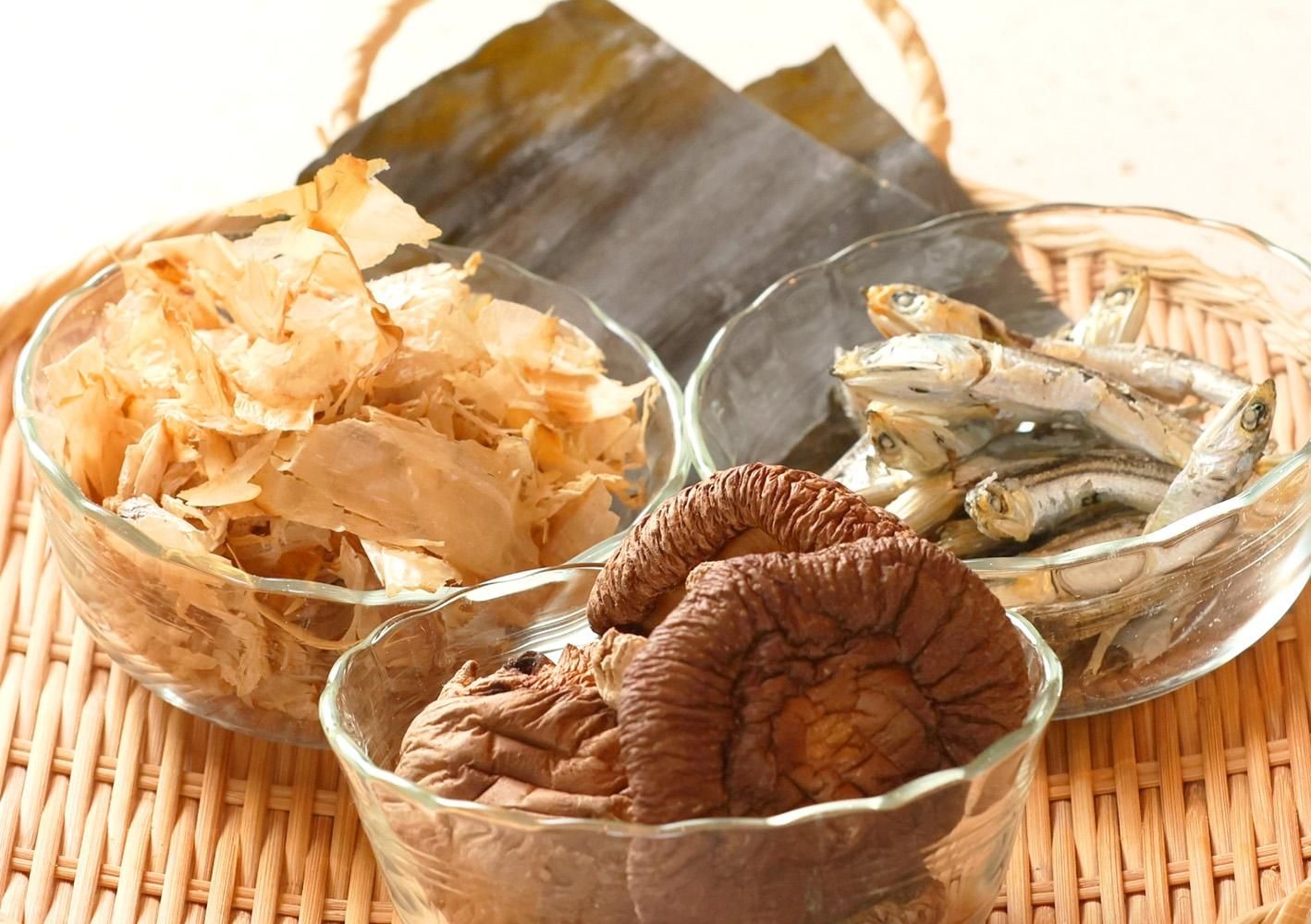 竹かごに並ぶ4種類のだし素材。かつお節、煮干し、干ししいたけ、奥に昆布