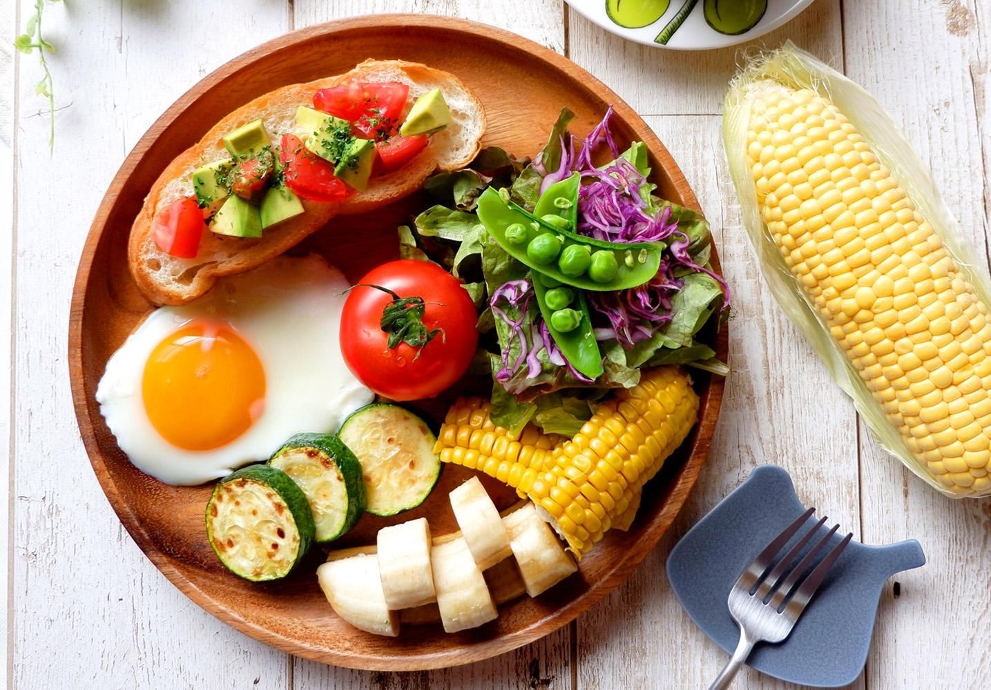 夏野菜を使った食卓の一例。木のプレートにトマト、ズッキーニ、コーン、サラダなどが盛られている
