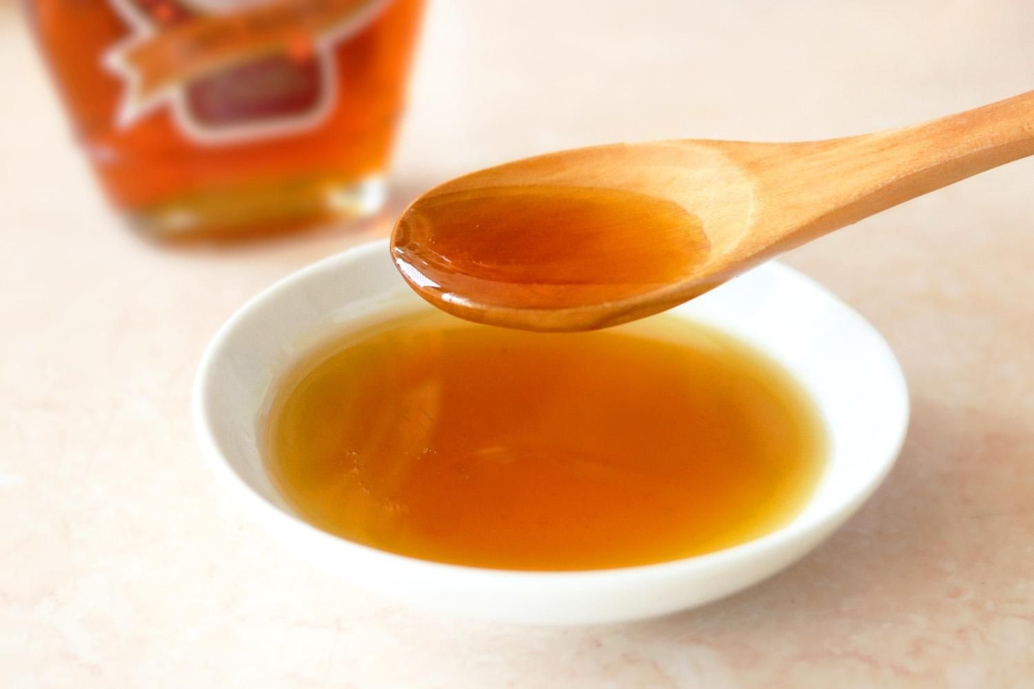 木のスプーンですくった琥珀色のはちみつと、小皿に入ったはちみつ