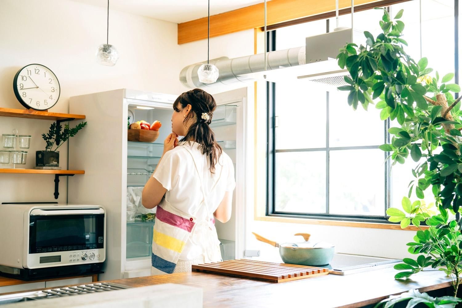エプロン姿の人が冷蔵庫を開けて中の食品を確かめている様子